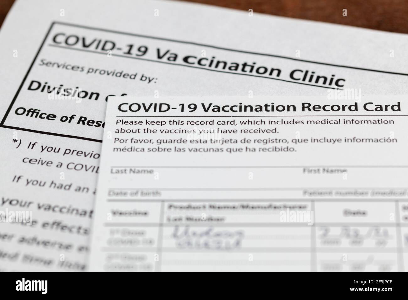 Primo piano immagine isolata di una scheda di registrazione delle vaccinazioni COVID 19 su una scrivania di legno. La carta indica la data, il tipo e il numero di dose del vca somministrato Foto Stock
