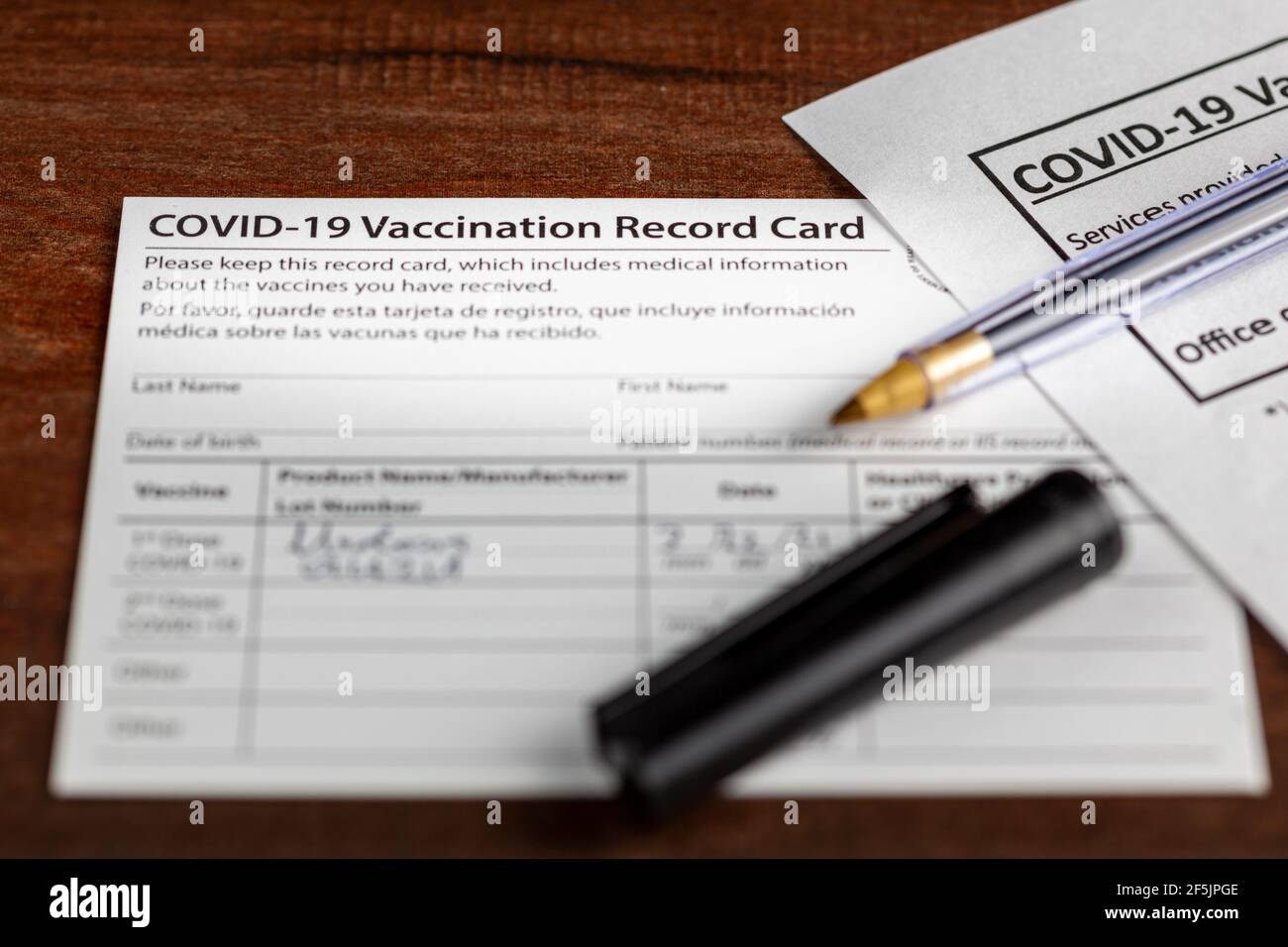 Primo piano immagine isolata di una scheda di registrazione delle vaccinazioni COVID 19 su una scrivania di legno. La scheda riporta la data, il tipo e il numero di dose di va somministrato Foto Stock