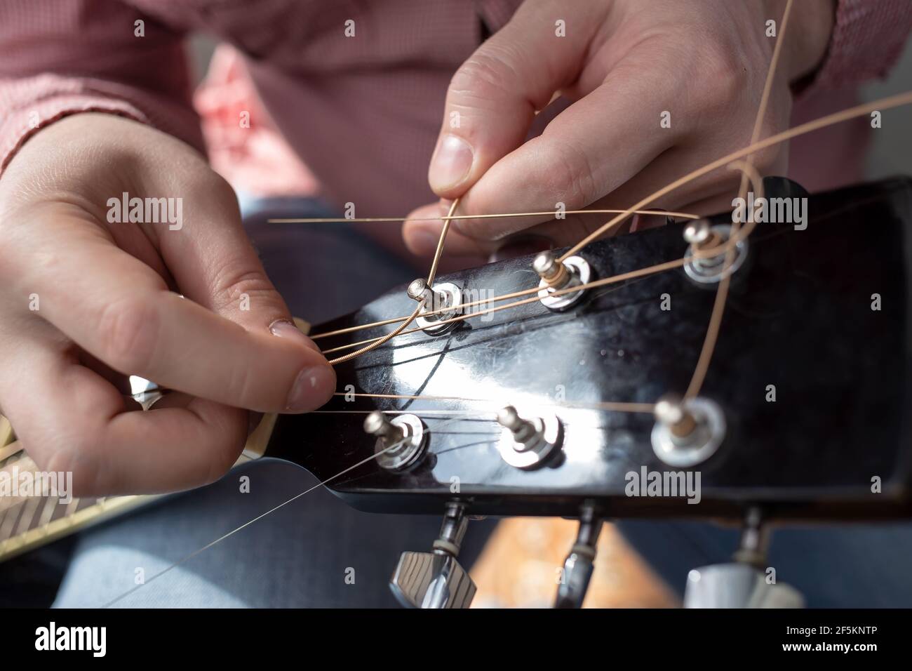 Mani maschio inserisce nuove corde in una chitarra acustica. Riparazione di strumenti musicali. Foto Stock