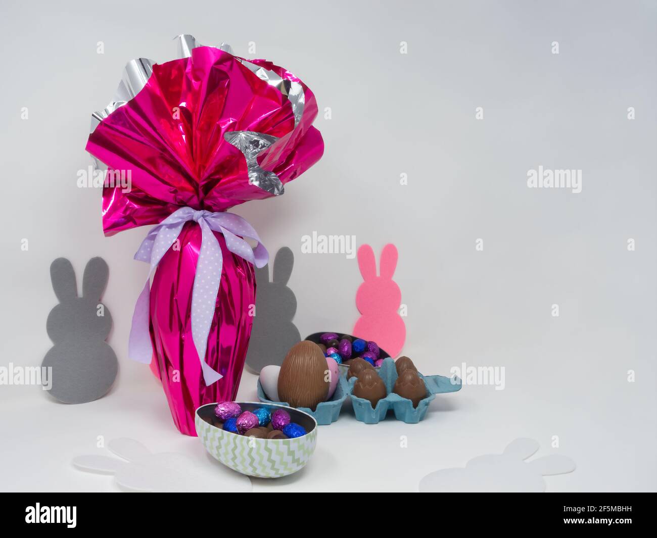 Uovo di Pasqua gigante con un nastro viola, piccole uova di cioccolato e altri cioccolatini. Sfondo vuoto Foto Stock