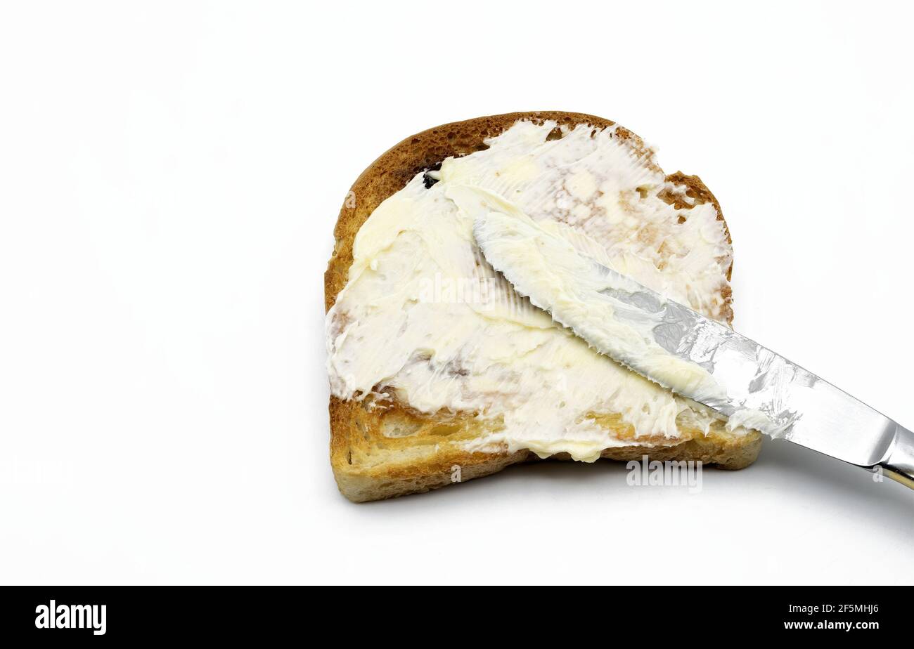 Spalmare il burro con un coltello sul pane tostato isolato su bianco sfondo Foto Stock