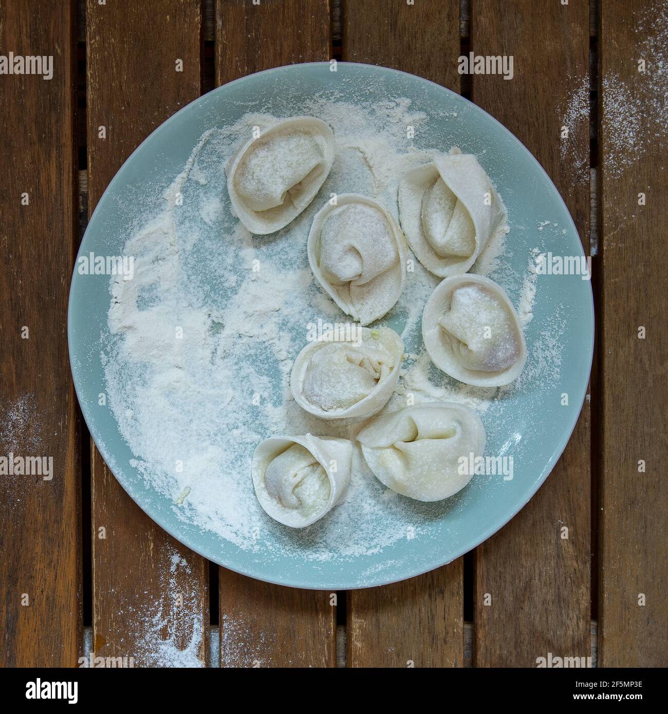 Gnocchi grezzi fatti a mano con farina su un piatto blu chiaro su un tavolo di legno scuro. Foto Stock