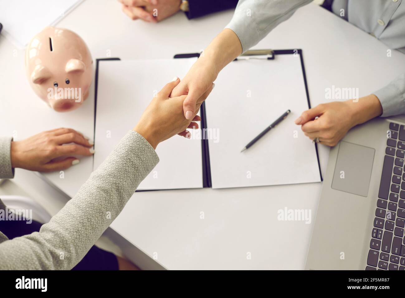 Closeup handshake femminile su contratto e piggybank su scrivania Foto Stock