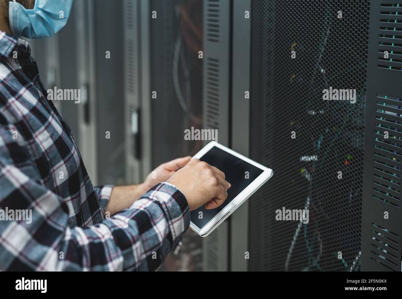 Ingegnere informatico maschile che lavora all'interno del database della sala server mentre si indossa maschera facciale durante l'epidemia di virus corona Foto Stock