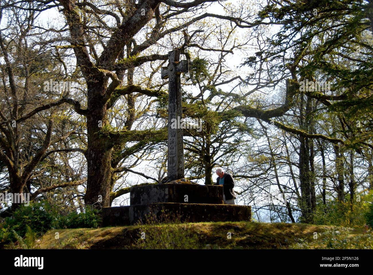 Uomo in piedi da solo con la testa piegata prima di una croce pubblica all'aperto in un bosco isolato, St Conan's Kirk, Loch AWe, Scozia Foto Stock