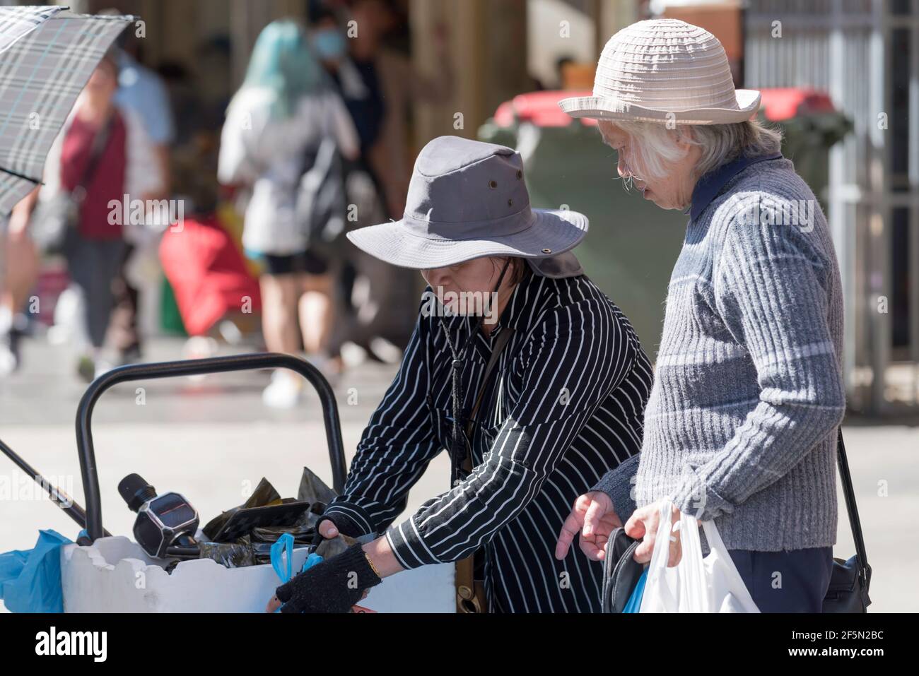 Una donna australiana vietnamita più anziana acquista verdure per strada A Sydney's Cabramatta da un'altra donna illegalmente commercio di strada Foto Stock