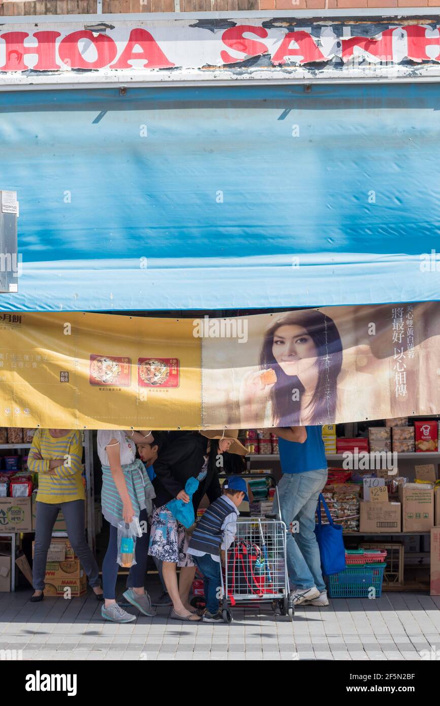 Una bandiera grande che prova ombra ad un negozio ha un faccia sorridente di una donna che si allinea comodamente Qualcuno che cammina dietro la bandiera a Cabramatta Foto Stock