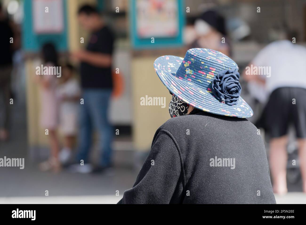 Una donna australiana vietnamita più anziana nella Cabramatta di Sydney, che indossa una maschera e un cappello da sole da dietro Foto Stock