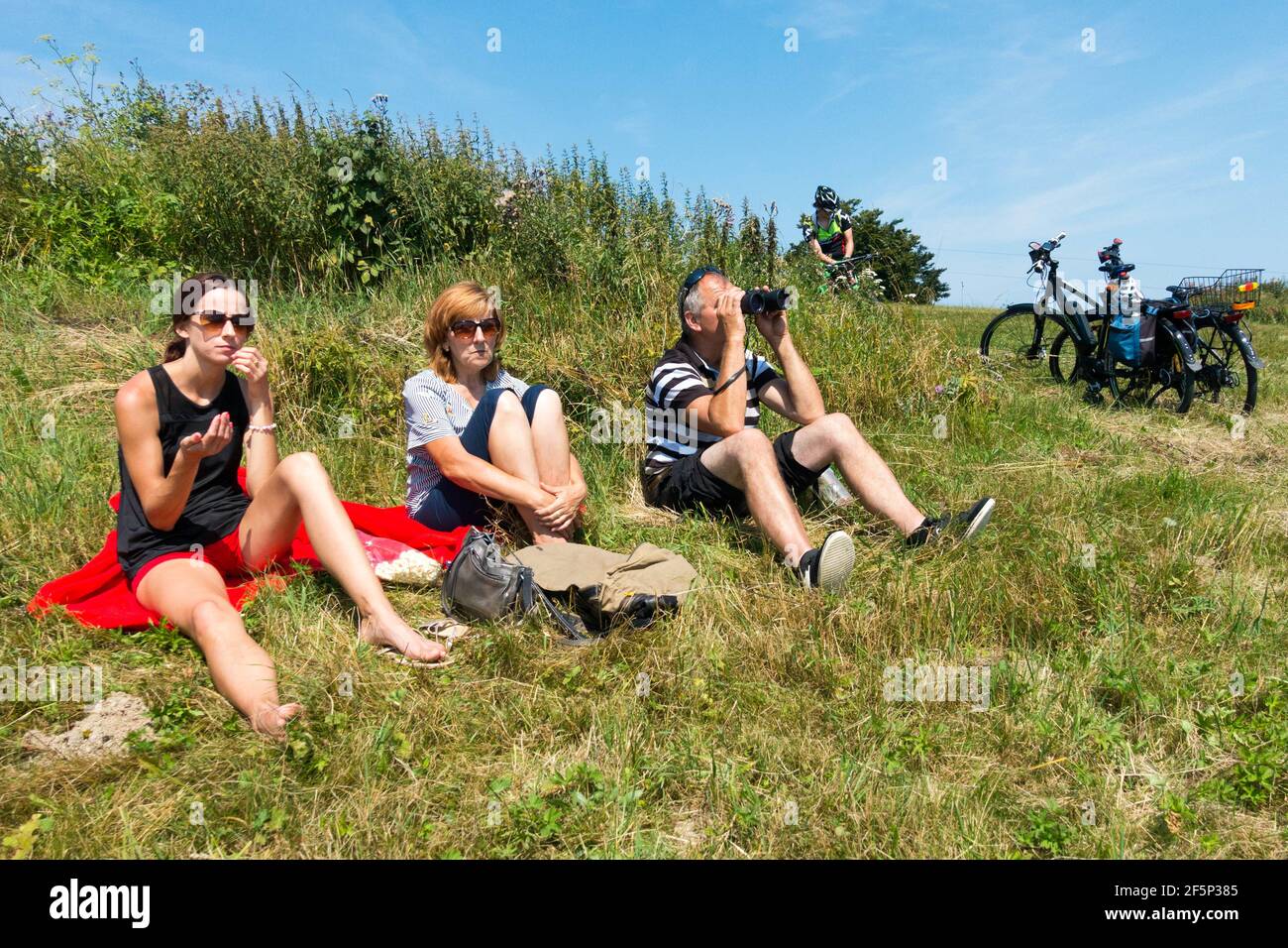 Tre ciclisti riposano in un prato, due donne e un uomo con binocoli Foto Stock