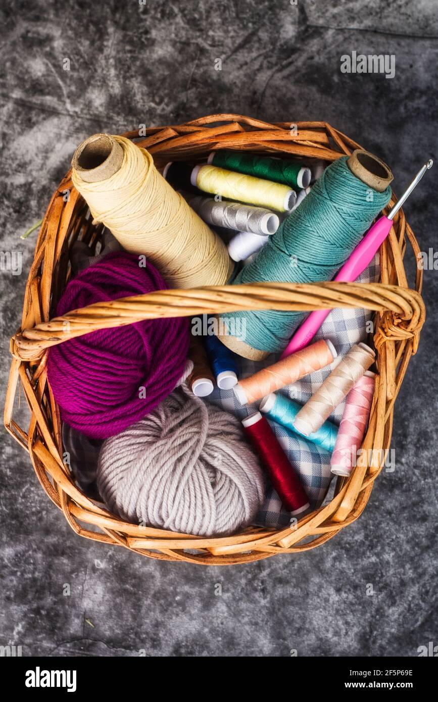 Cesto pieno di fili colorati e palle di filato e. un gancio a crochet Foto Stock
