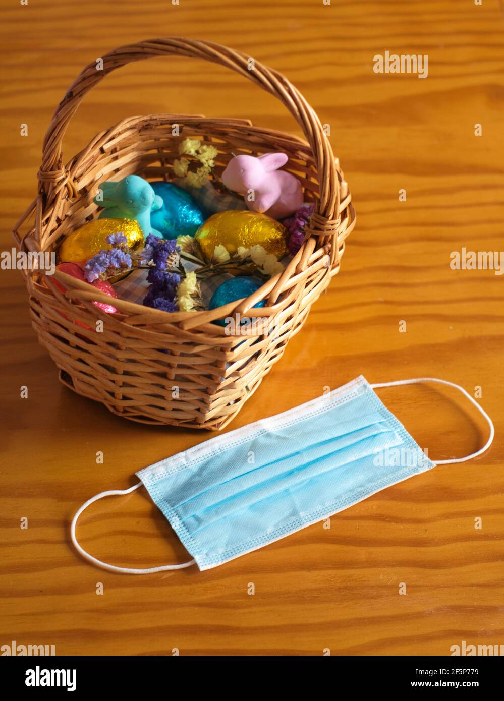 Cestino con uova di pasqua, conigli e fiori su un tavolo di legno. Maschera facciale all'esterno del cestello Foto Stock