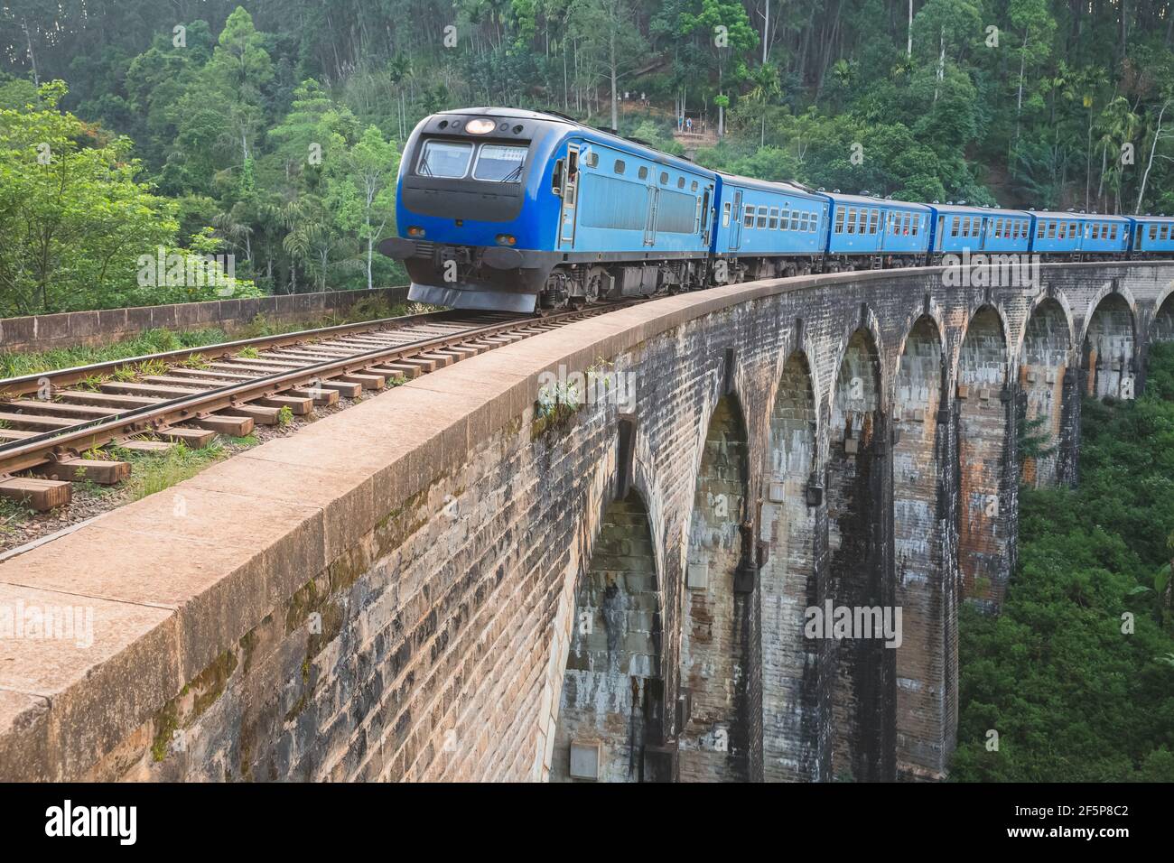 Un treno blu attraversa il viadotto del Ponte Demodara Nine Arches passando attraverso la regione collinare della giungla dello Sri Lanka in un viaggio panoramico. Foto Stock