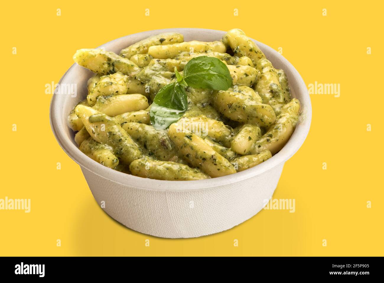 Gnocchi con salsa al pesto genovese in cartoncino da asporto, isolati su fondo giallo Foto Stock