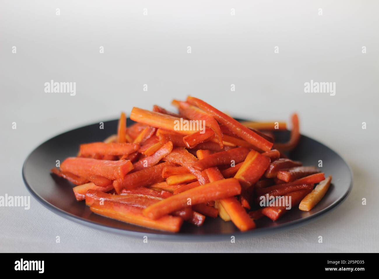 Bastoncini di carote caramellate. Carote salate con burro e zucchero. Uno spuntino veloce e sano. Scatto su sfondo bianco Foto Stock