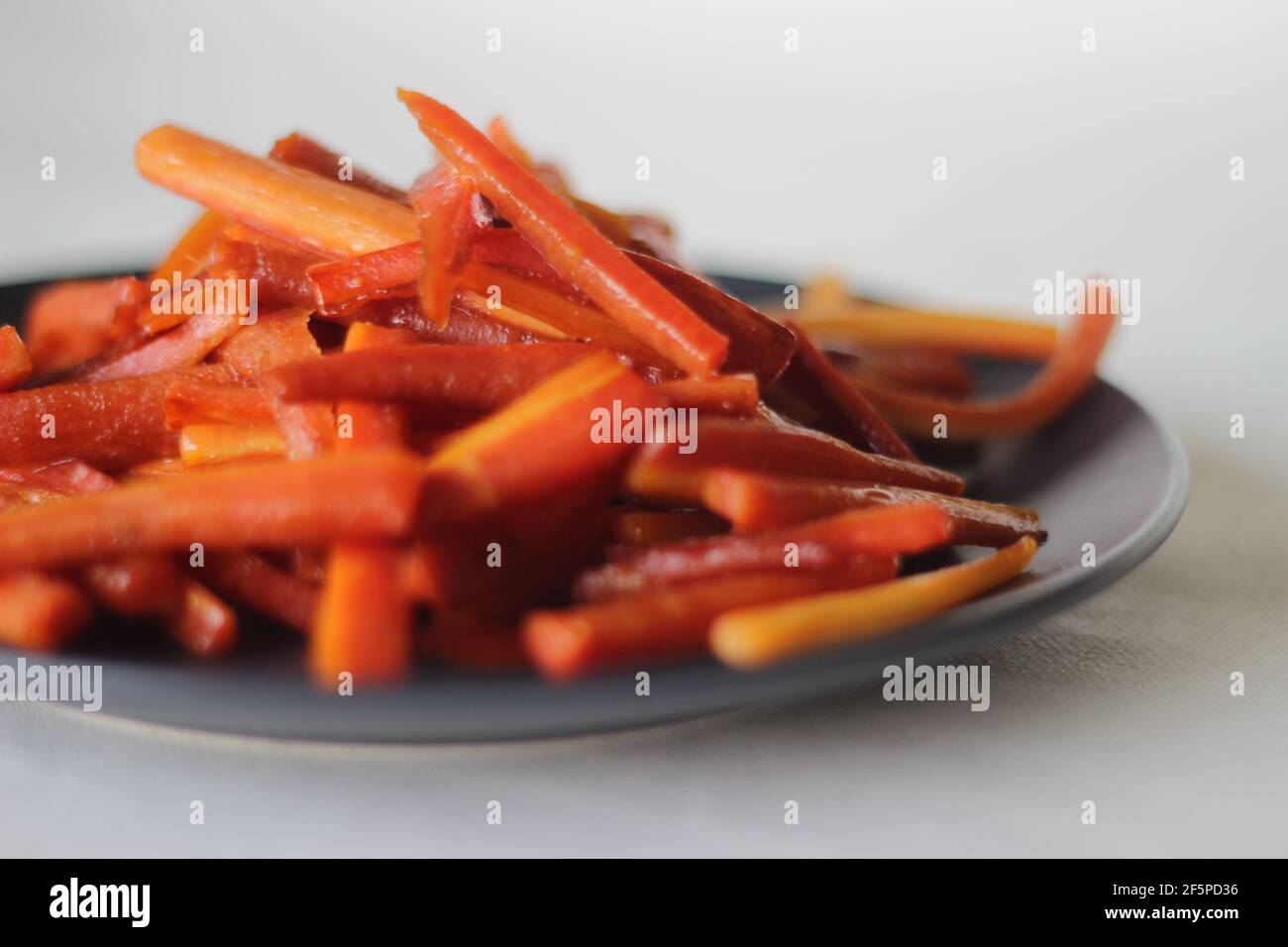 Bastoncini di carote caramellate. Carote salate con burro e zucchero. Uno spuntino veloce e sano. Scatto su sfondo bianco Foto Stock