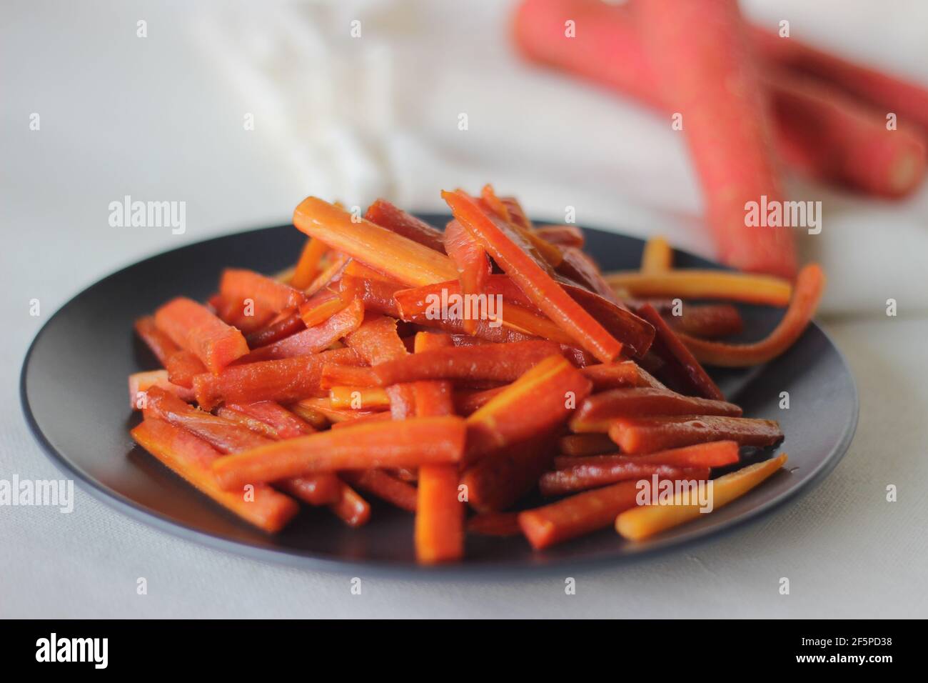 Bastoncini di carote caramellate. Carote salate con burro e zucchero. Uno spuntino veloce e sano. Scatto su sfondo bianco Foto Stock