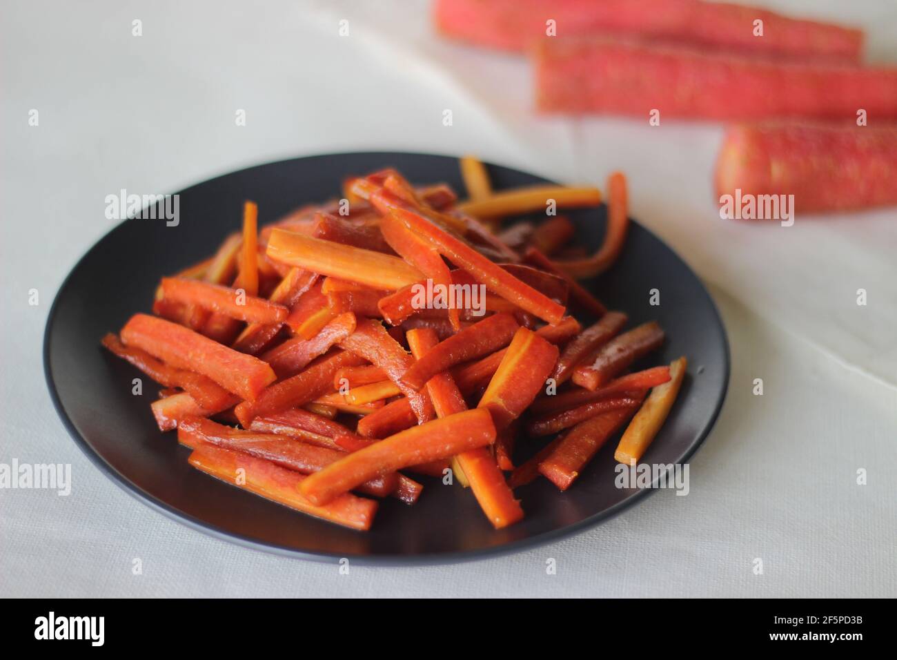 Bastoncini di carote caramellate. Carote salate con burro e zucchero. Uno spuntino veloce e sano. Scatto su sfondo bianco Foto Stock