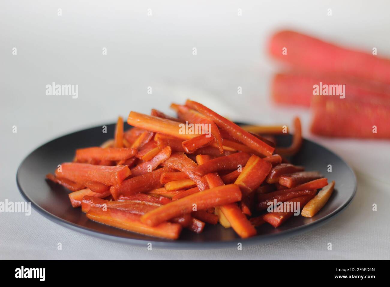 Bastoncini di carote caramellate. Carote salate con burro e zucchero. Uno spuntino veloce e sano. Scatto su sfondo bianco Foto Stock