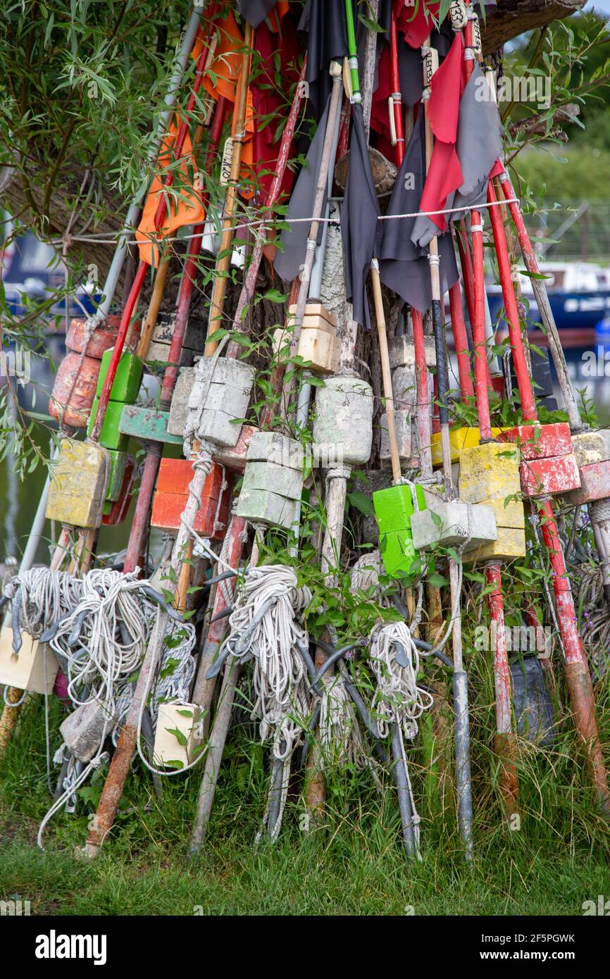 Pali e bandiere per marcare trappole di pesce si appoggiano contro un albero nel porticciolo di Zempin sull'isola di Usedom. Foto Stock