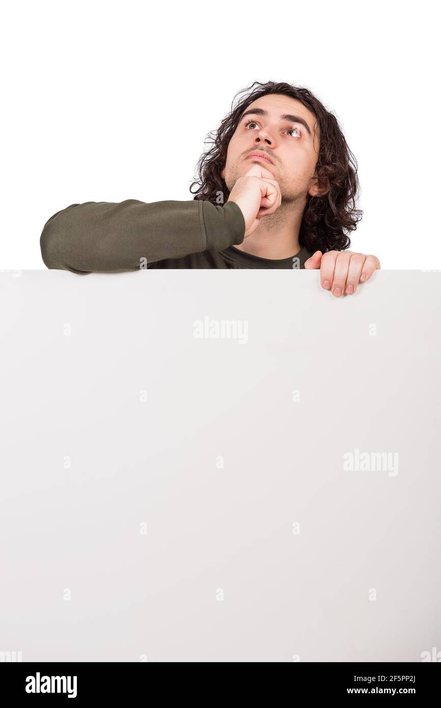 Meditando il giovane, si trova dietro un banner vuoto, guardando in alto pensieroso. Foglio vuoto con spazio di copia per pubblicità e messaggi. Pensiva e focosa Foto Stock