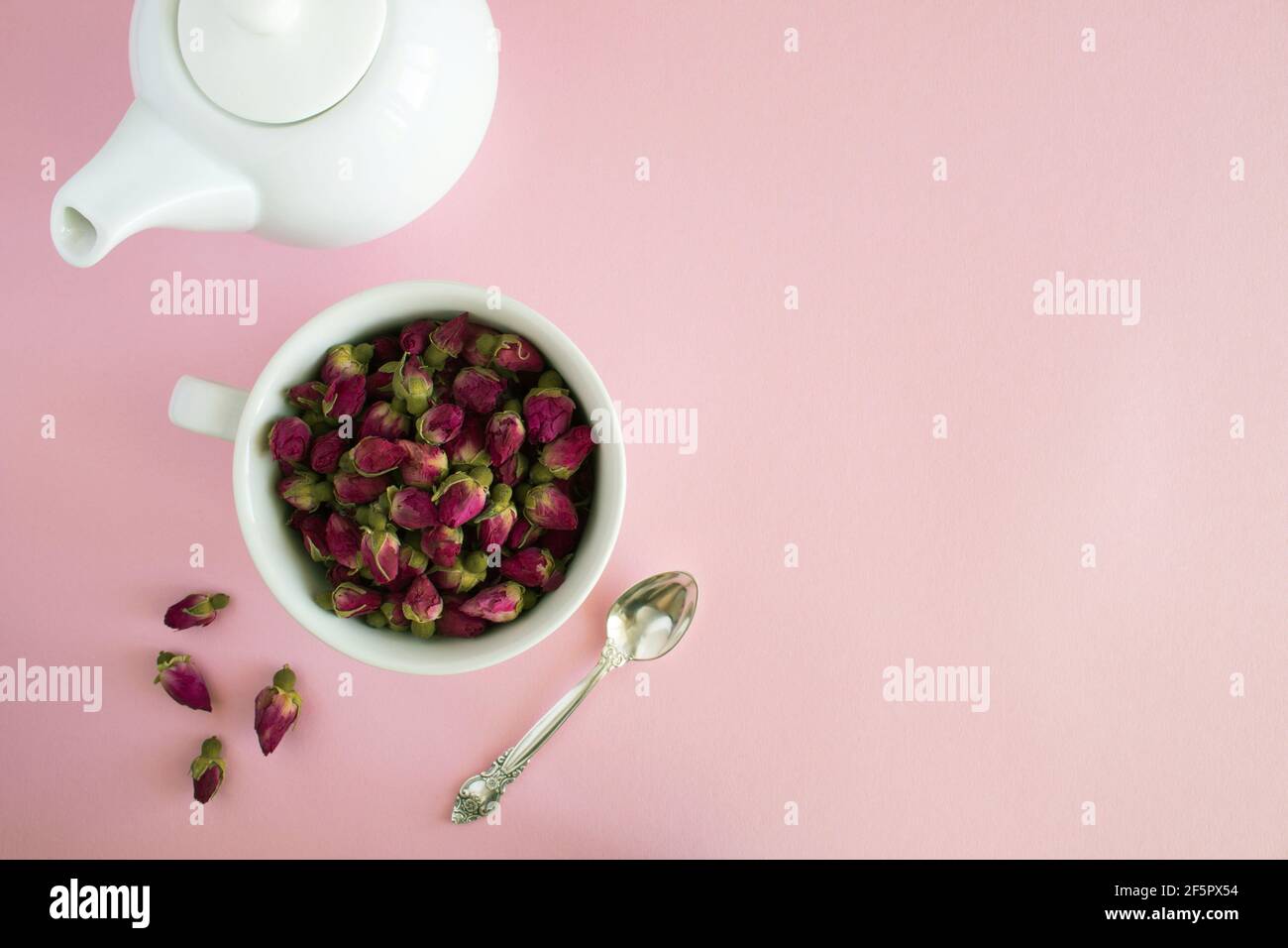 Asciugare le rose rosa nella tazza bianca e preparare il bollitore su sfondo rosa.Copia spazio.Vista dall'alto. Foto Stock