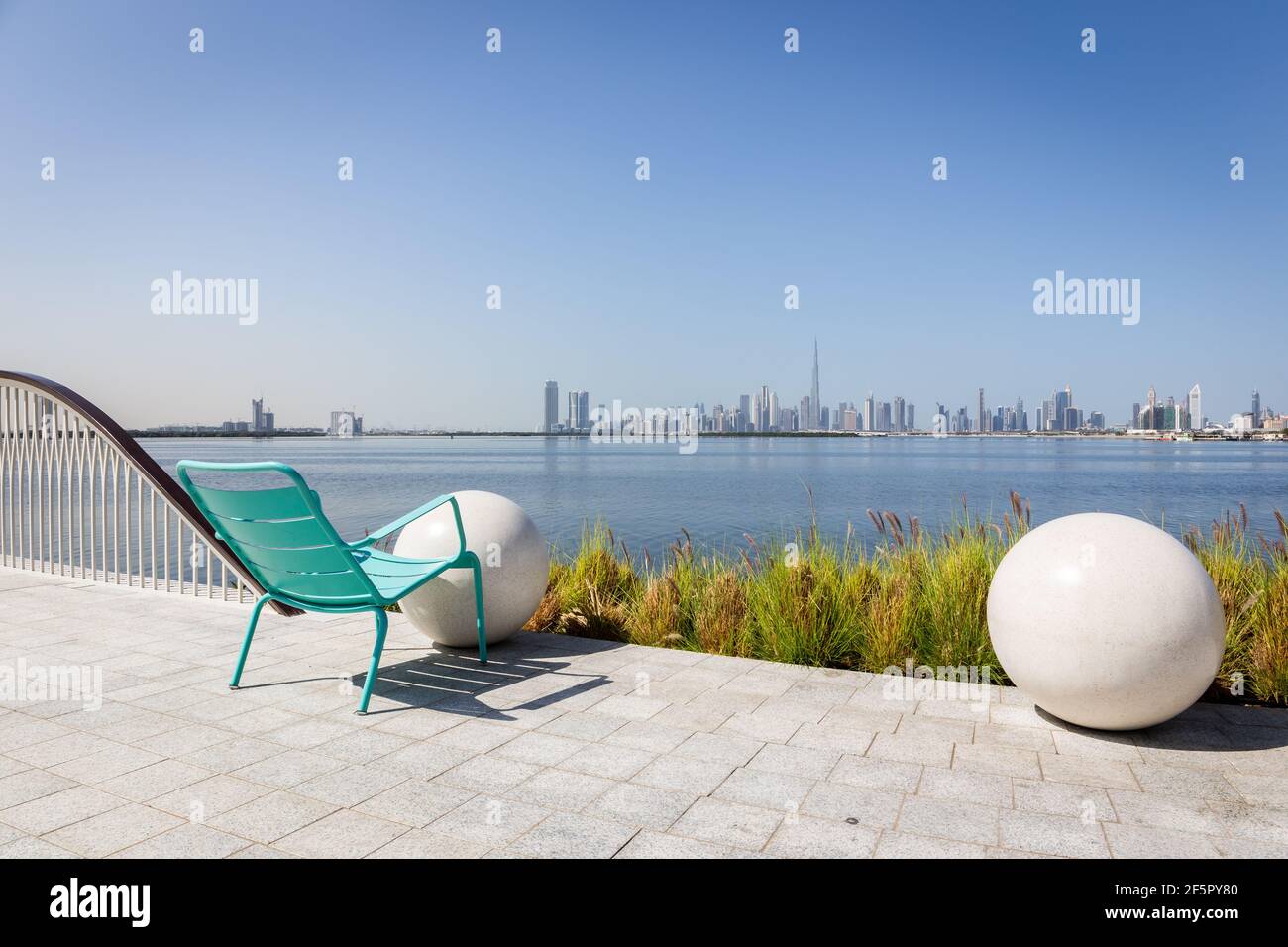 Dubai, Emirati Arabi Uniti, 22.02.2021. Sedia verde su una passeggiata che si affaccia sul centro di Dubai con l'edificio Burj Khalifa e il Dubai Creek, il Dubai Creek Harbour, Emirati Arabi Uniti Foto Stock