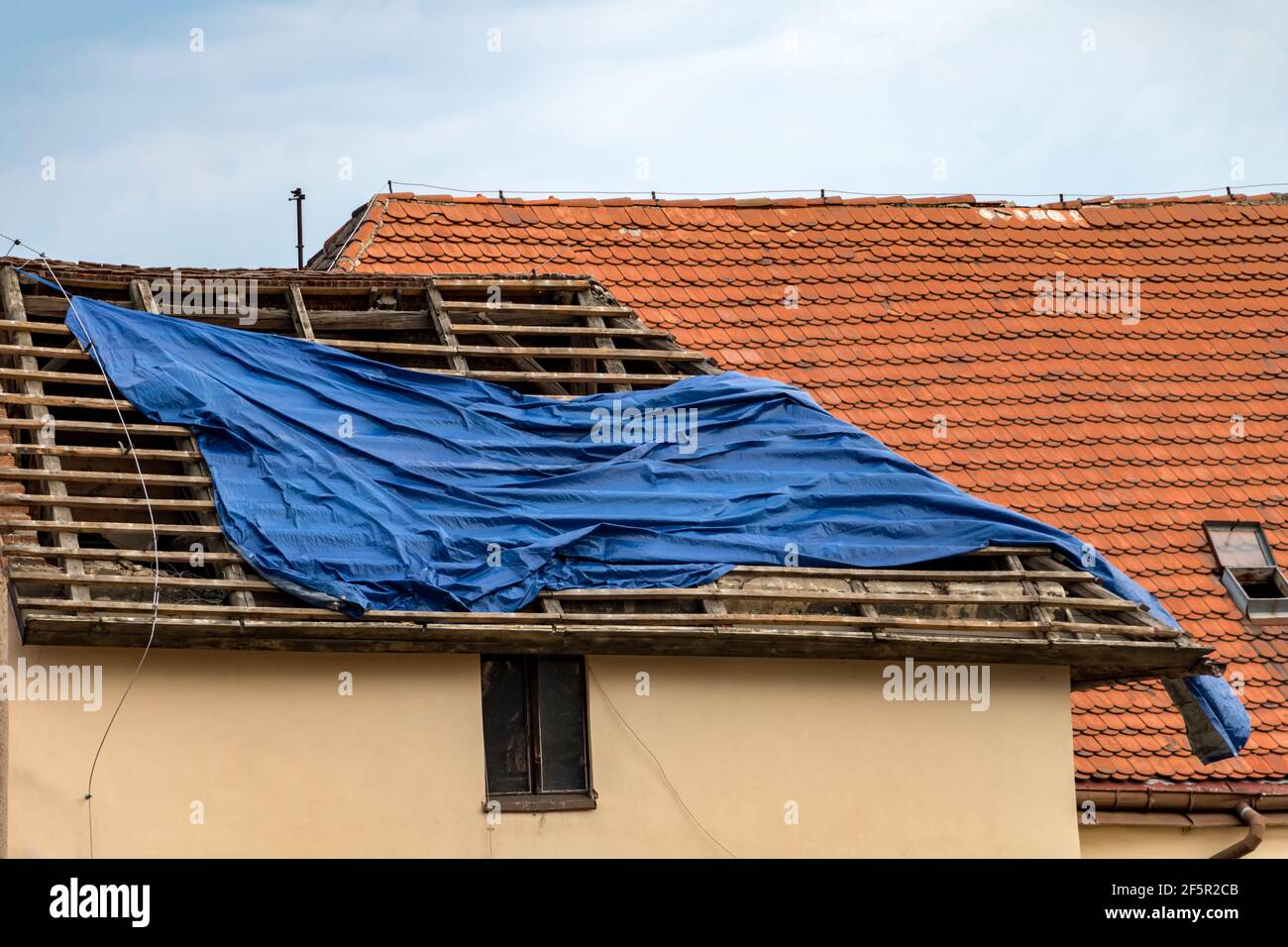 La tempesta ha danneggiato il fissaggio della copertura sul tetto.  Installazione di un telone protettivo sul tetto della casa in ricostruzione  Foto stock - Alamy