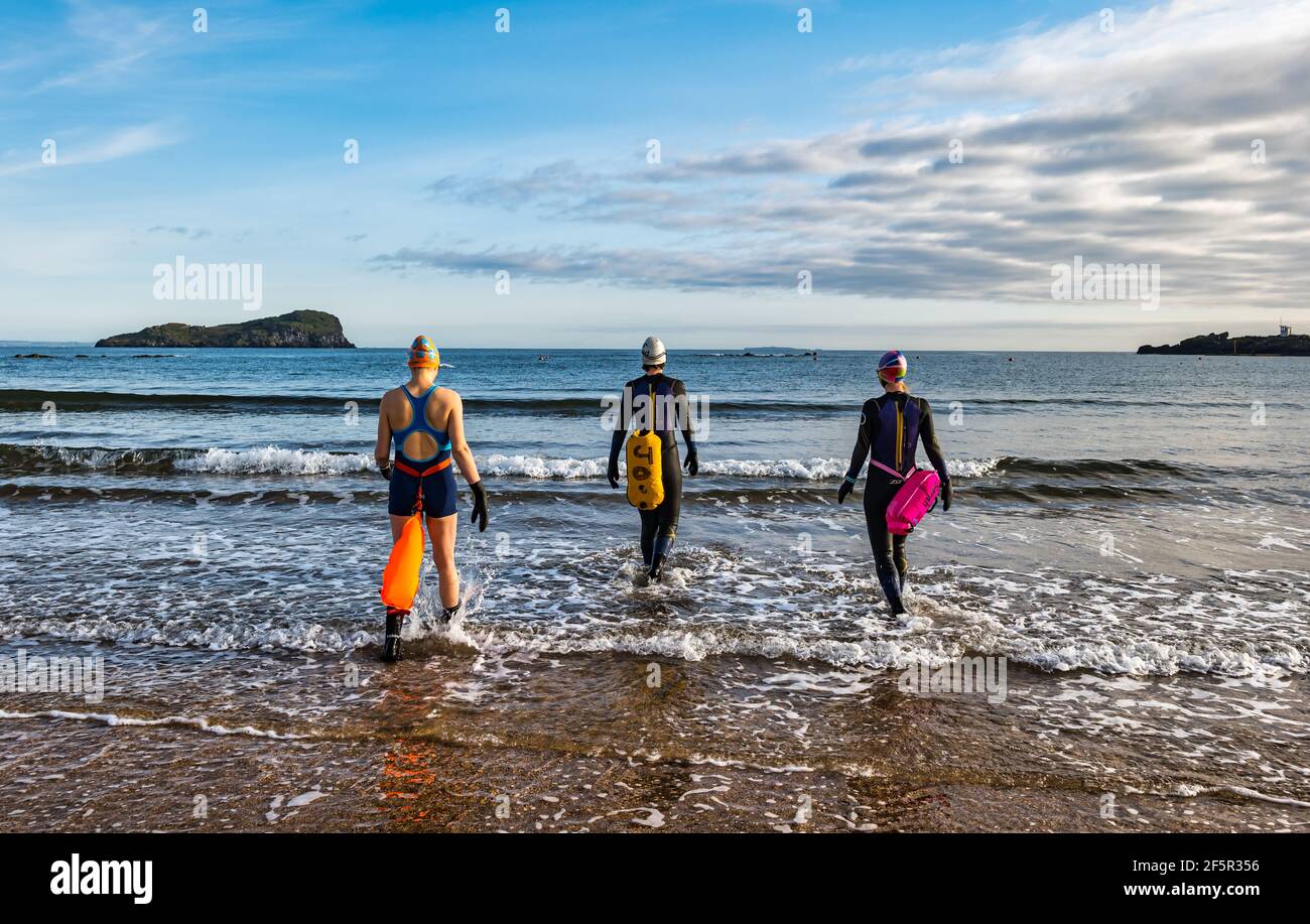 Le donne in mare aperto o selvaggio che indossano mute con galleggianti entrano nel Firth of Forth Sea, North Berwick, East Lothian, Scotland, UK Foto Stock