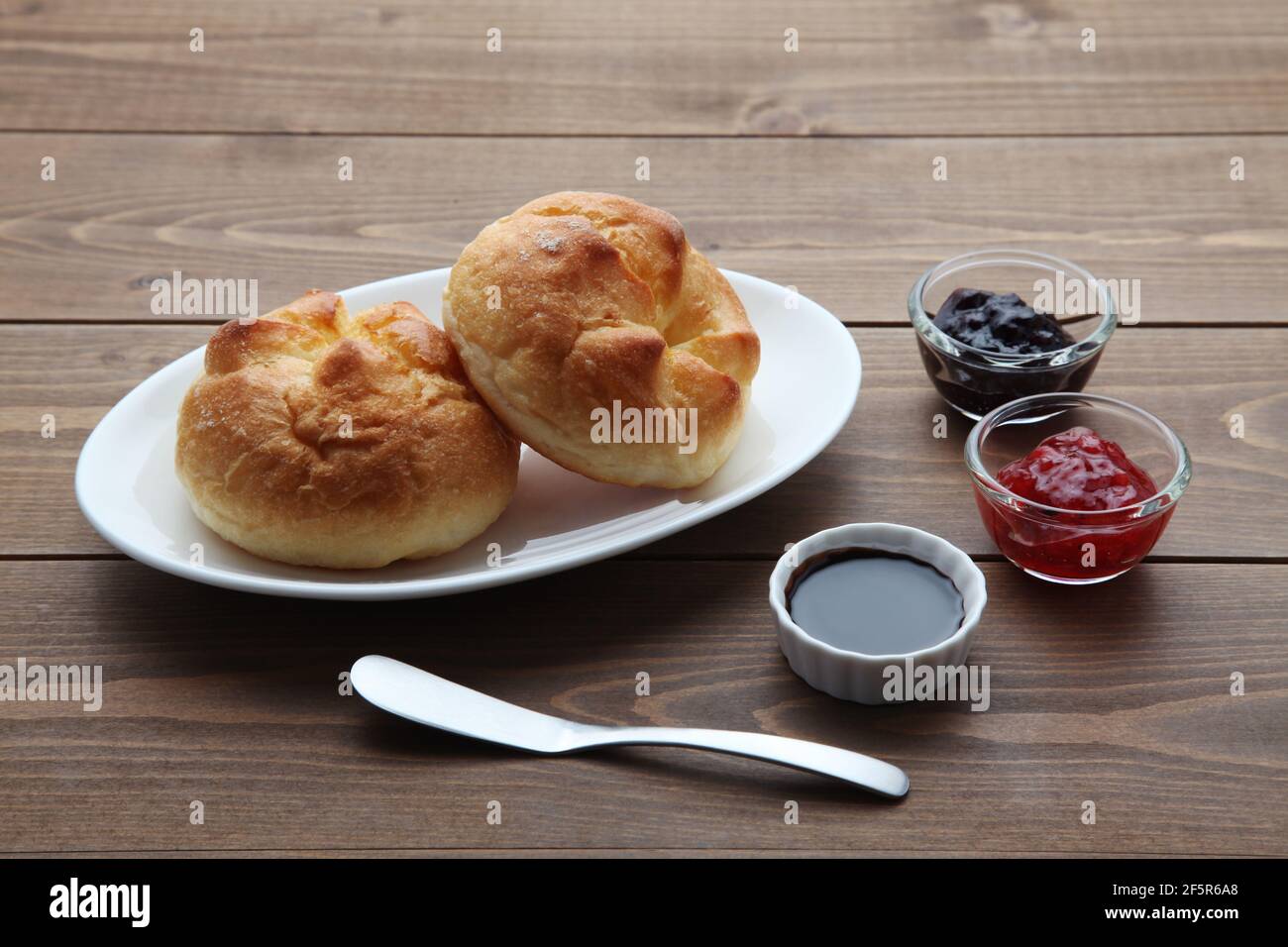 burro il rotolo di pane su un piatto con la marmellata di fragole sopra tavolo di legno Foto Stock