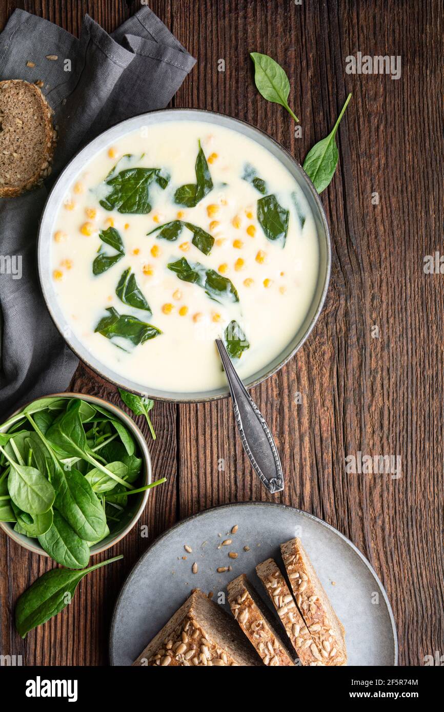 Zuppa cremosa di ceci e aglio con spinaci e purè di patate, servita con pane integrale su rustico fondo di legno Foto Stock