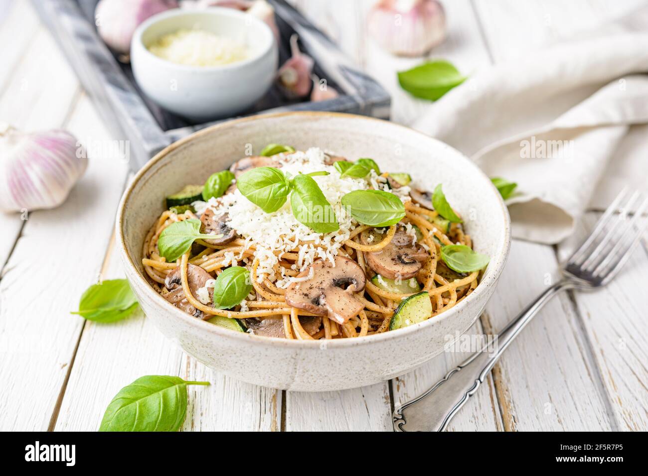 Sani spaghetti di grano integrale con aglio e zucchine di funghi saltati, conditi con formaggio grattugiato e foglie di basilico su rustico fondo di legno Foto Stock