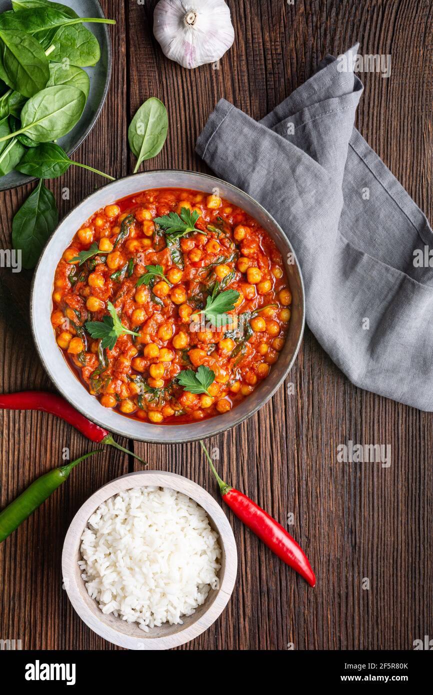 Pasto indiano, curry piccante di ceci con spinaci in una ciotola servita con riso su rustico fondo di legno Foto Stock