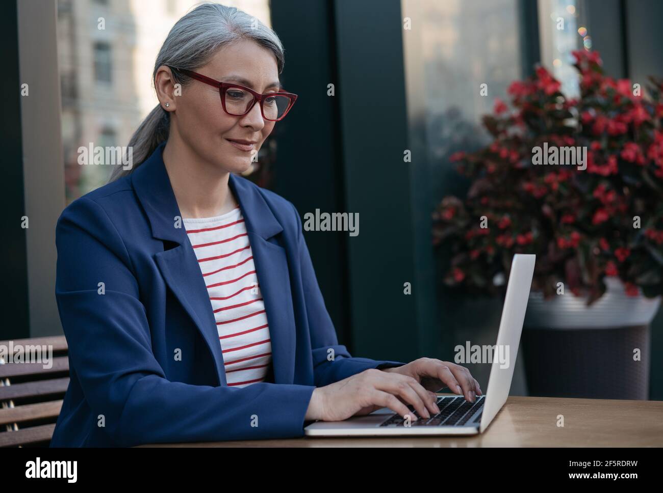 Donna d'affari matura che usa un computer portatile, che lavora online. Ritratto di copywriter asiatico di mezza età che indossa occhiali eleganti digitando sulla tastiera Foto Stock