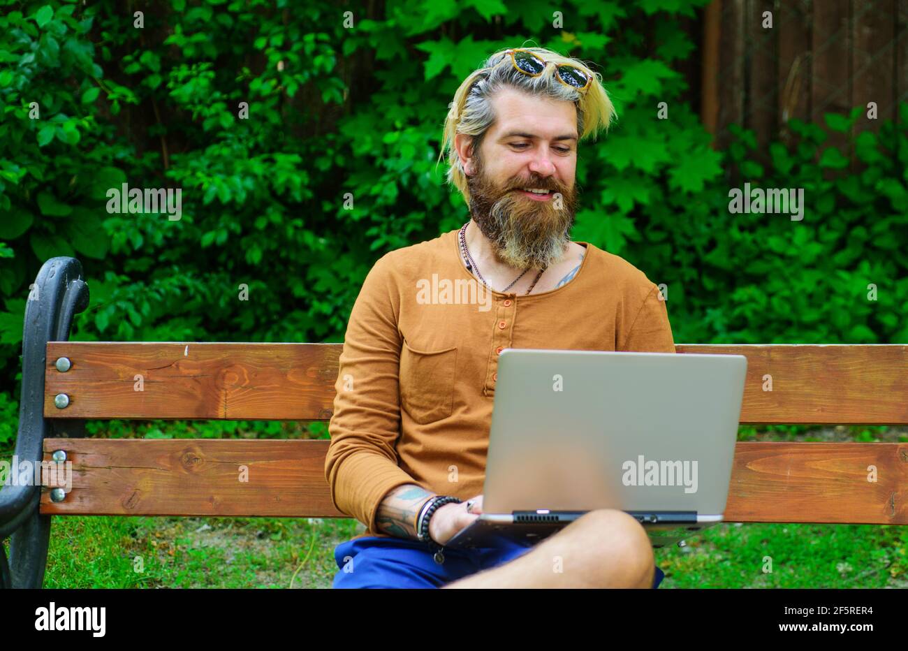 Uomo sorridente che lavora su un computer portatile all'aperto. Uomo d'affari con notebook al parco. Freelance. Studiare e lavorare online. Foto Stock