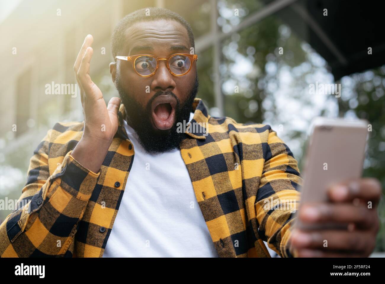Uomo scioccato a bocca aperta con il telefono cellulare, guardando lo schermo digitale. Ritratto di emotivo freelance afroamericano mancato scadenza Foto Stock