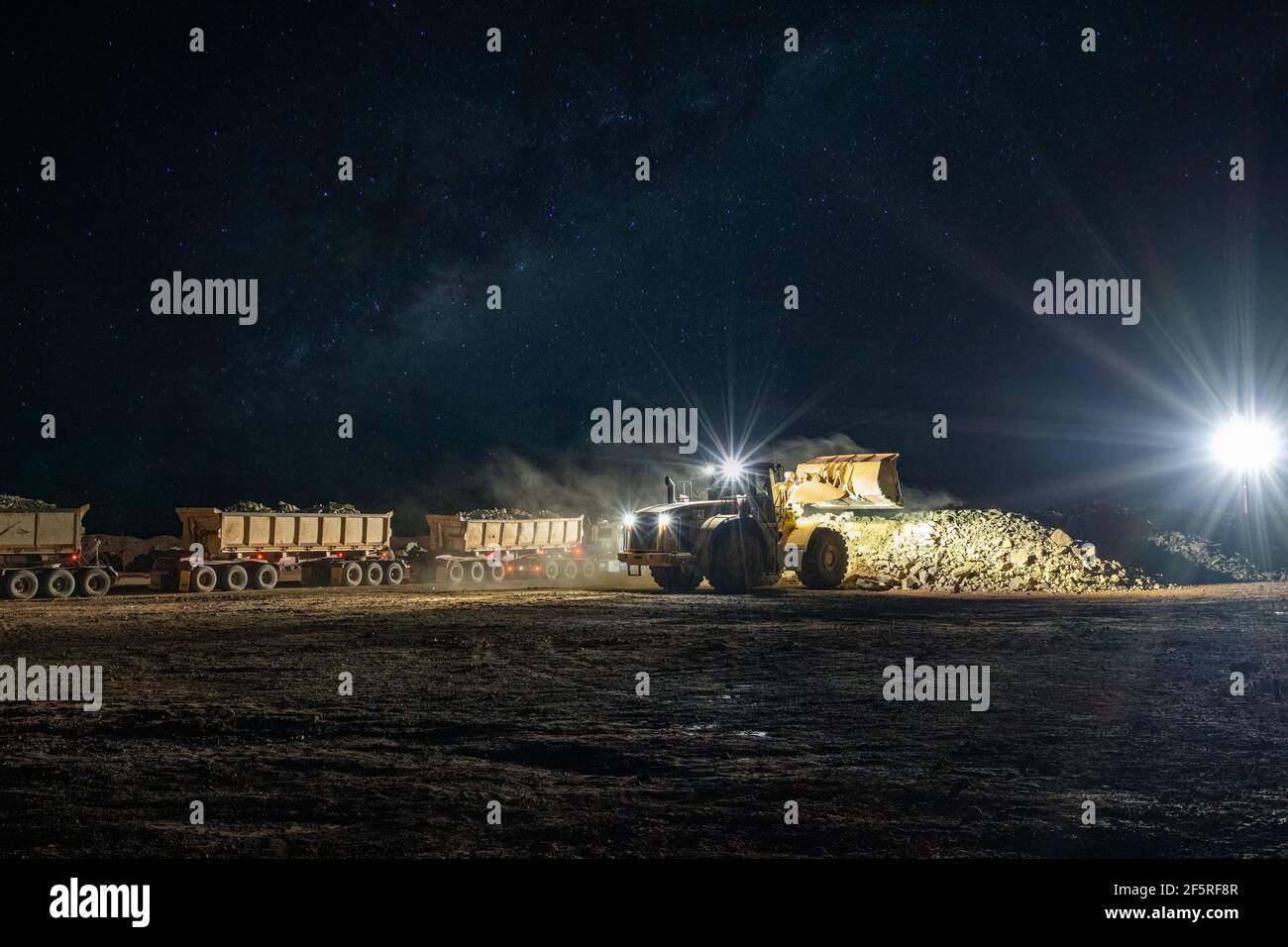 Attività di estrazione a cielo aperto di notte con carri di perforazione, dumper e caricatori che operano sotto i proiettori. Foto Stock