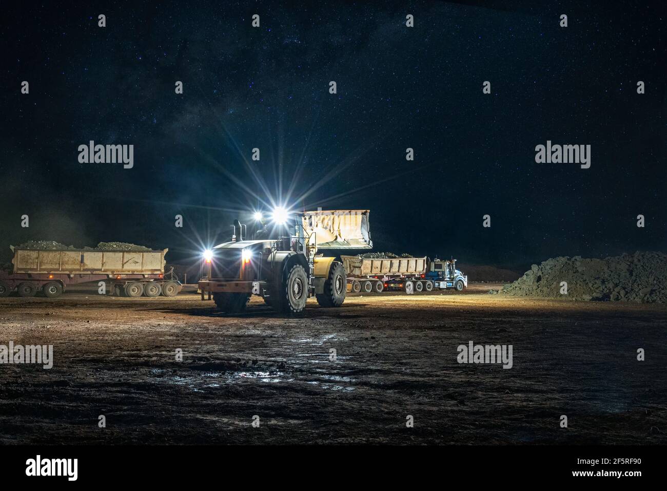 Attività di estrazione a cielo aperto di notte con carri di perforazione, dumper e caricatori che operano sotto i proiettori. Foto Stock