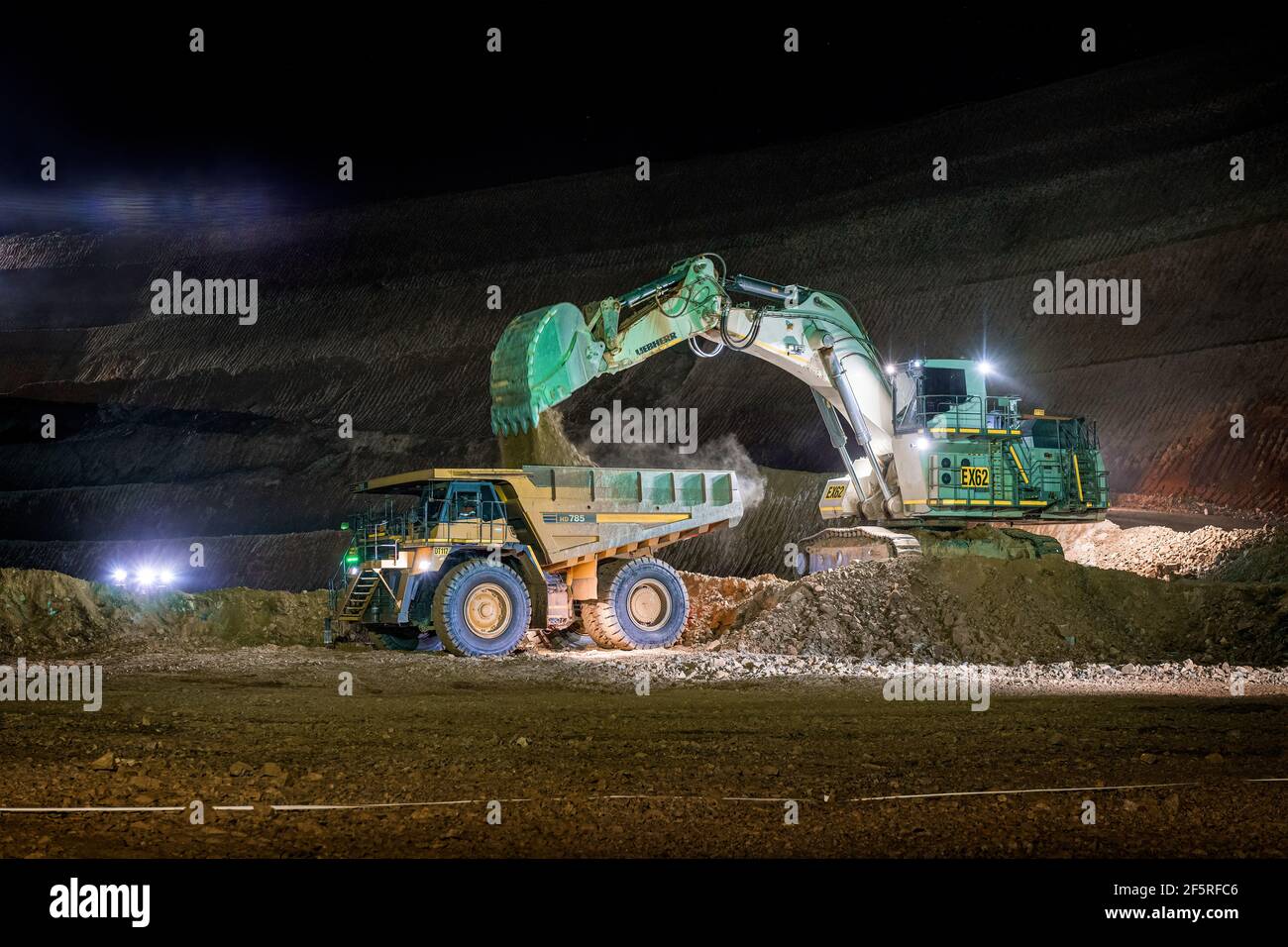 Attività di estrazione a cielo aperto di notte con carri di perforazione, dumper e caricatori che operano sotto i proiettori. Foto Stock