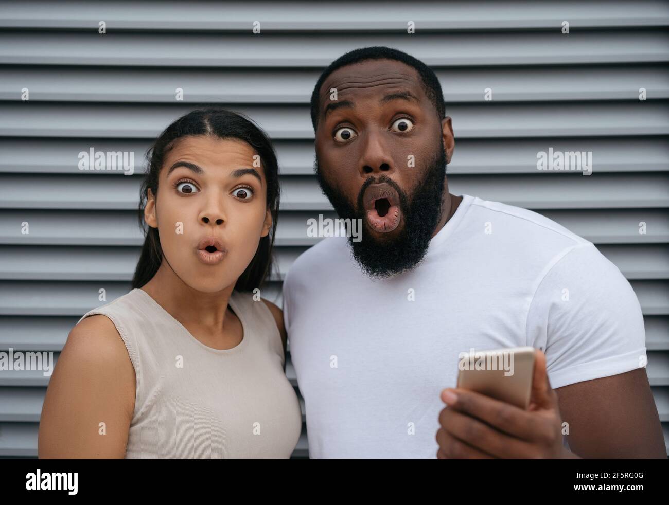 Eccitato afroamericano uomo e donna che tiene il telefono cellulare, shopping online guardando la macchina fotografica. Concetto di scommesse sportive Foto Stock