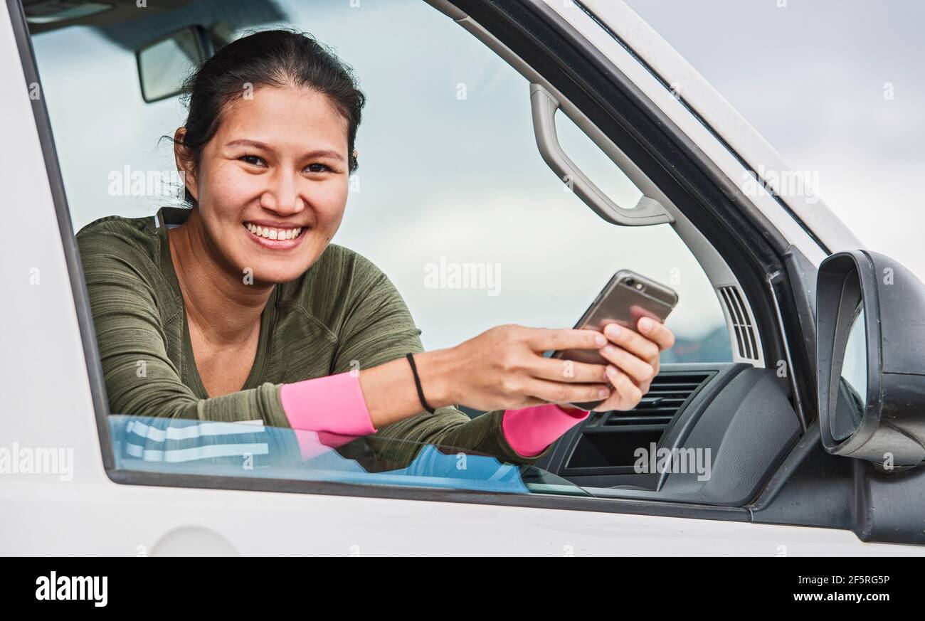 Donna che sta testando sul suo smartphone mentre si siede nel suo furgone Foto Stock