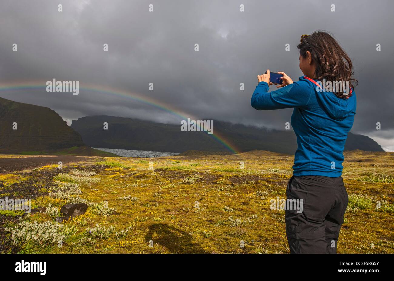 Donna scattando foto sul suo smartphone di arcobaleno in Icland Foto Stock