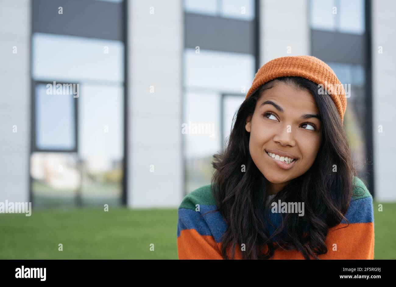 Bella donna afroamericana mordendo il suo labbro, pensando, cercando di copiare spazio, in piedi all'aperto Foto Stock