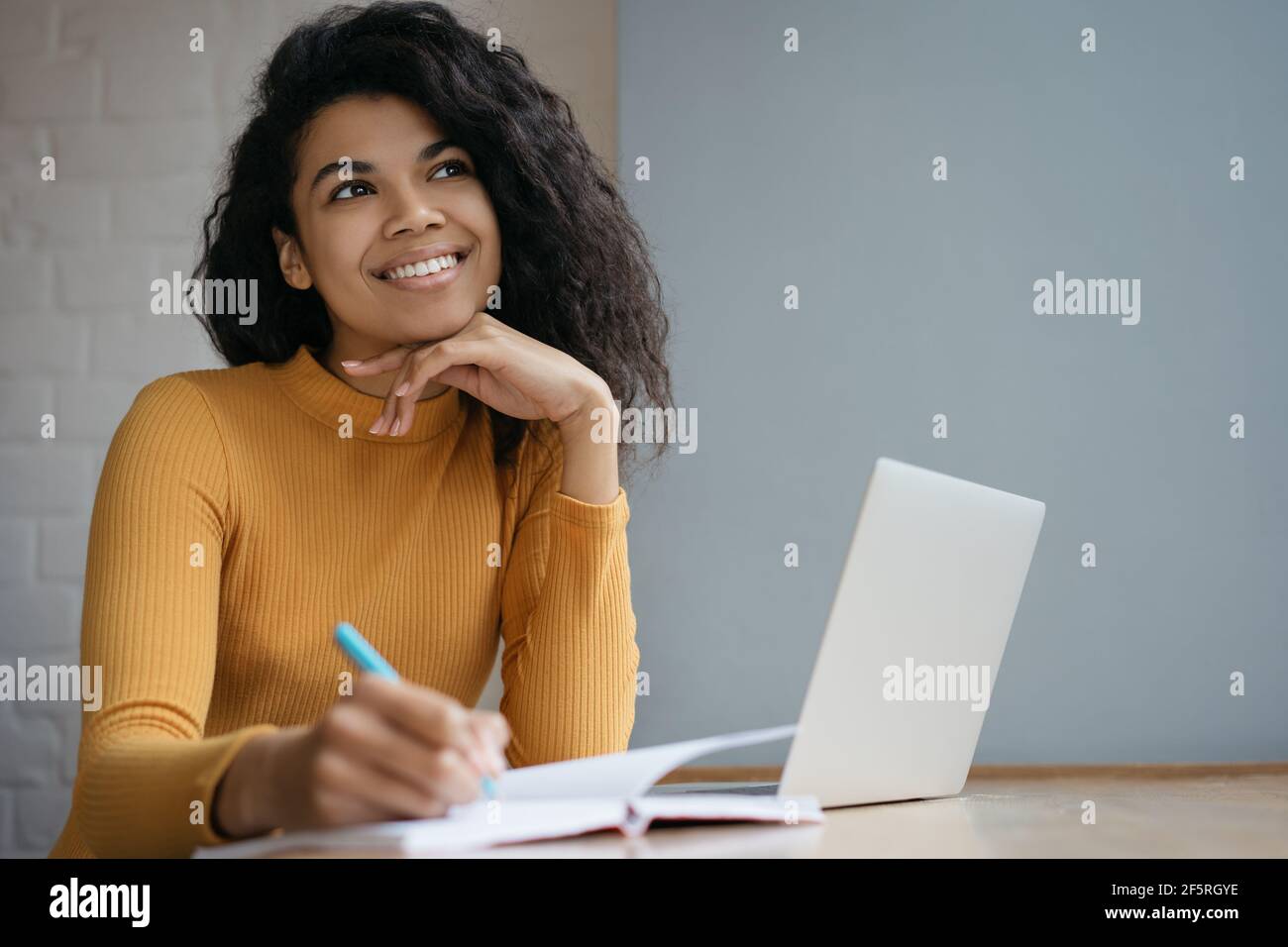 Ritratto di felice allievo pensivo che studia, preparazione all'esame, formazione in linea. Bella donna afroamericana prendendo appunti lavorando da casa Foto Stock