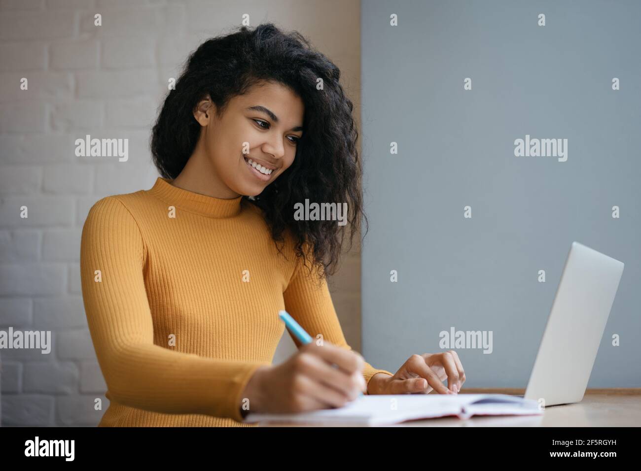 Studente afroamericano che studia, utilizzando un computer portatile, prendendo appunti su un notebook. Concetto di formazione online. Giovane bella donna che lavora da casa Foto Stock