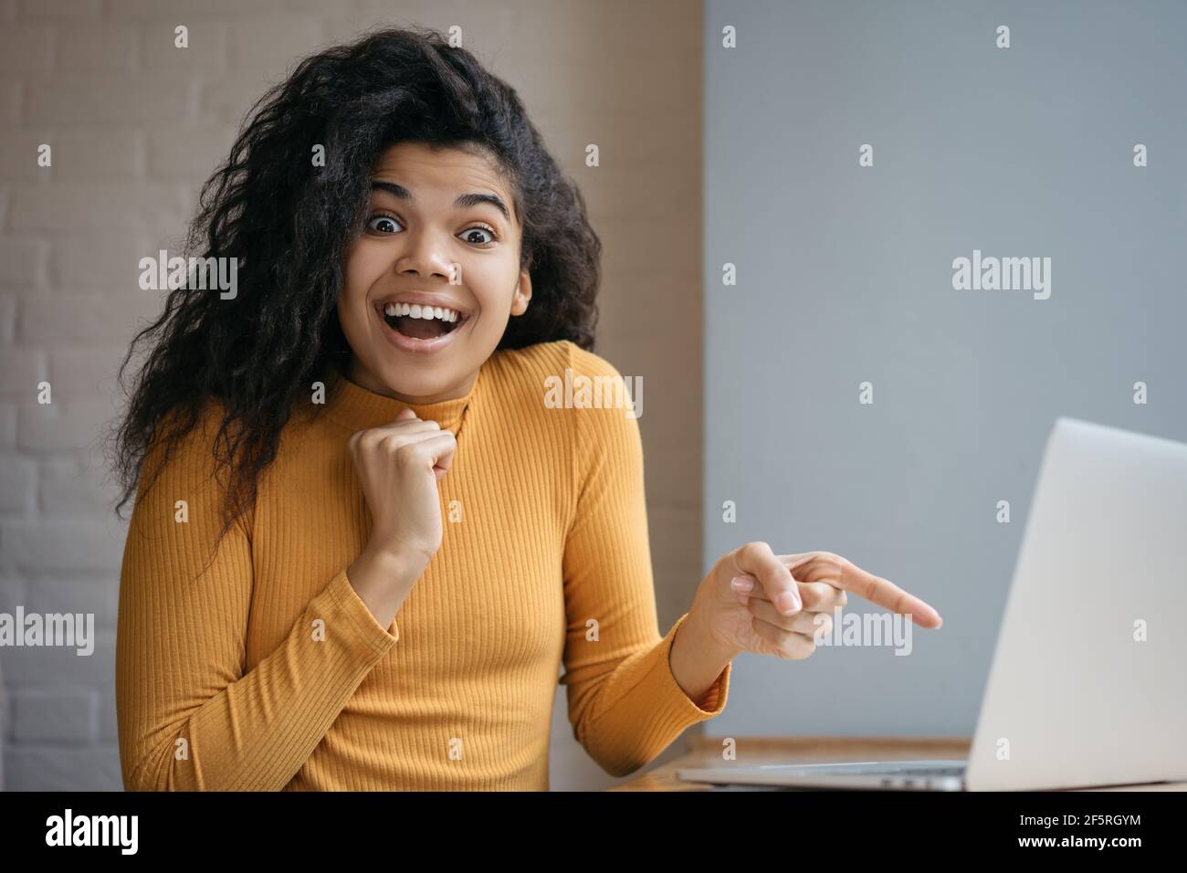 Donna afroamericana sorpresa che mostra il dito sullo schermo del laptop. Ritratto di un influencer entusiasta che guarda la fotocamera a bocca aperta Foto Stock