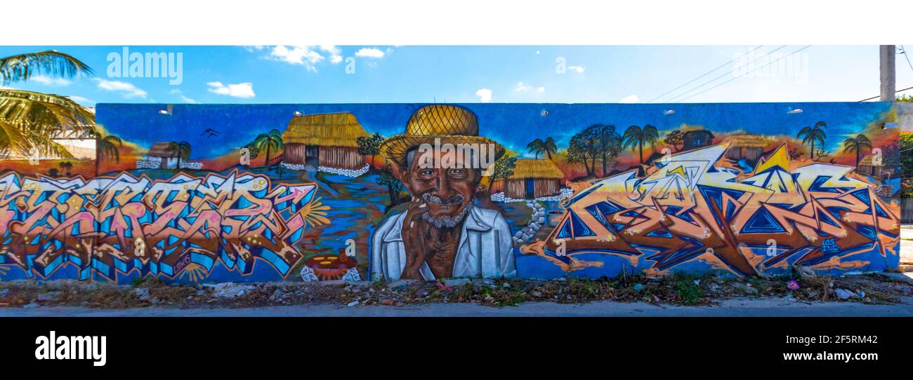 Arte di strada in una piccola città del Messico su una lunga parete con un vecchio uomo che indossa un cappello di paglia, una baita rustica e parole, con un cielo blu sopra il muro Foto Stock