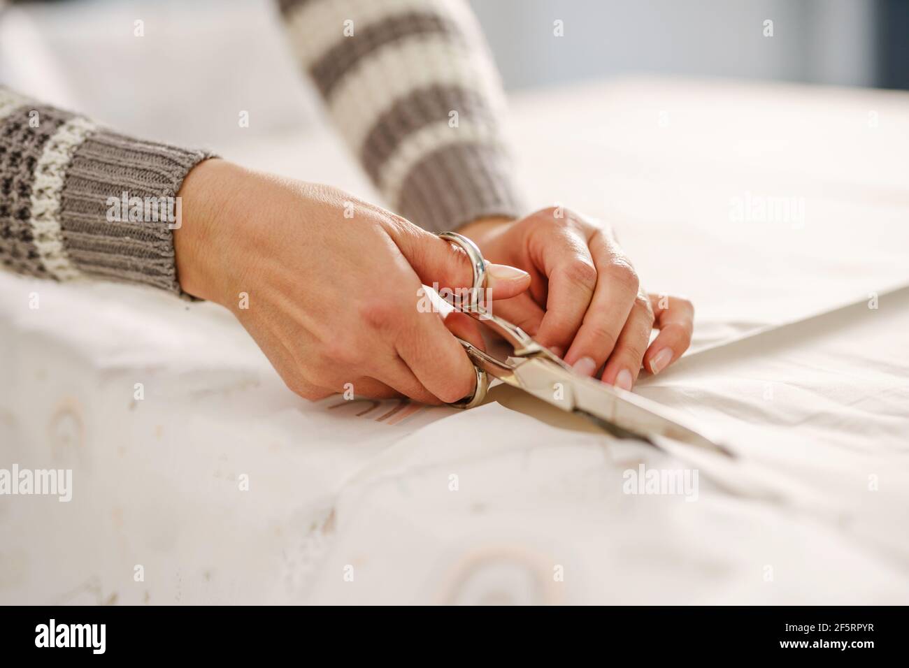 Primo piano sulle mani di una donna caucasica sconosciuta che tiene forbici taglio di tessuti sul tavolo a casa o in studio - hobby e concetto di sartoring Foto Stock