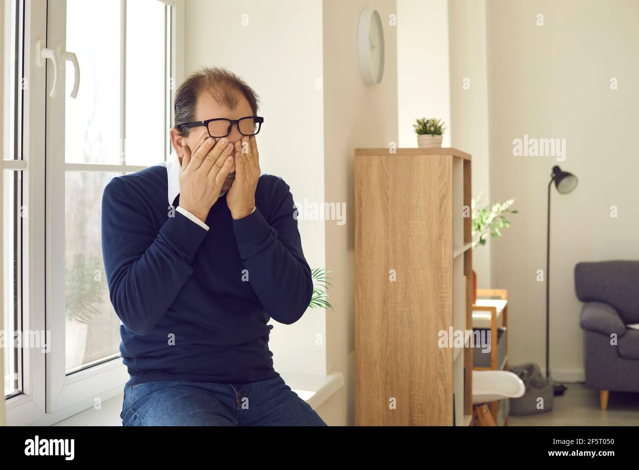 Ritratto di uomo maturo che indossa occhiali che sfregano gli occhi seduti davanzale Foto Stock