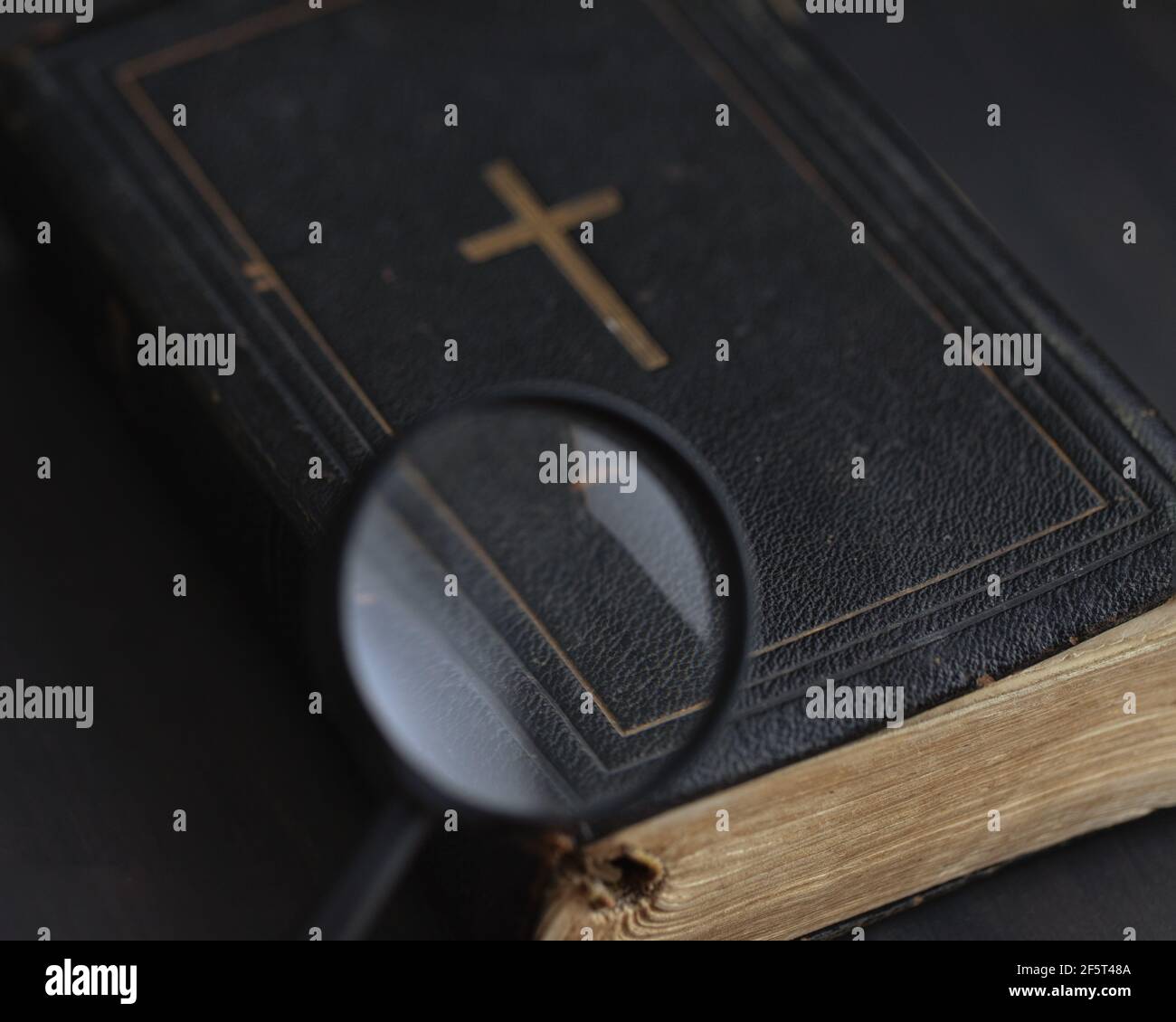 Chiusa Bibbia antica in pelle nera copertina con croce d'oro al centro e pagine giallastre è visto attraverso la lente di ingrandimento su sfondo nero. Ricerca Foto Stock