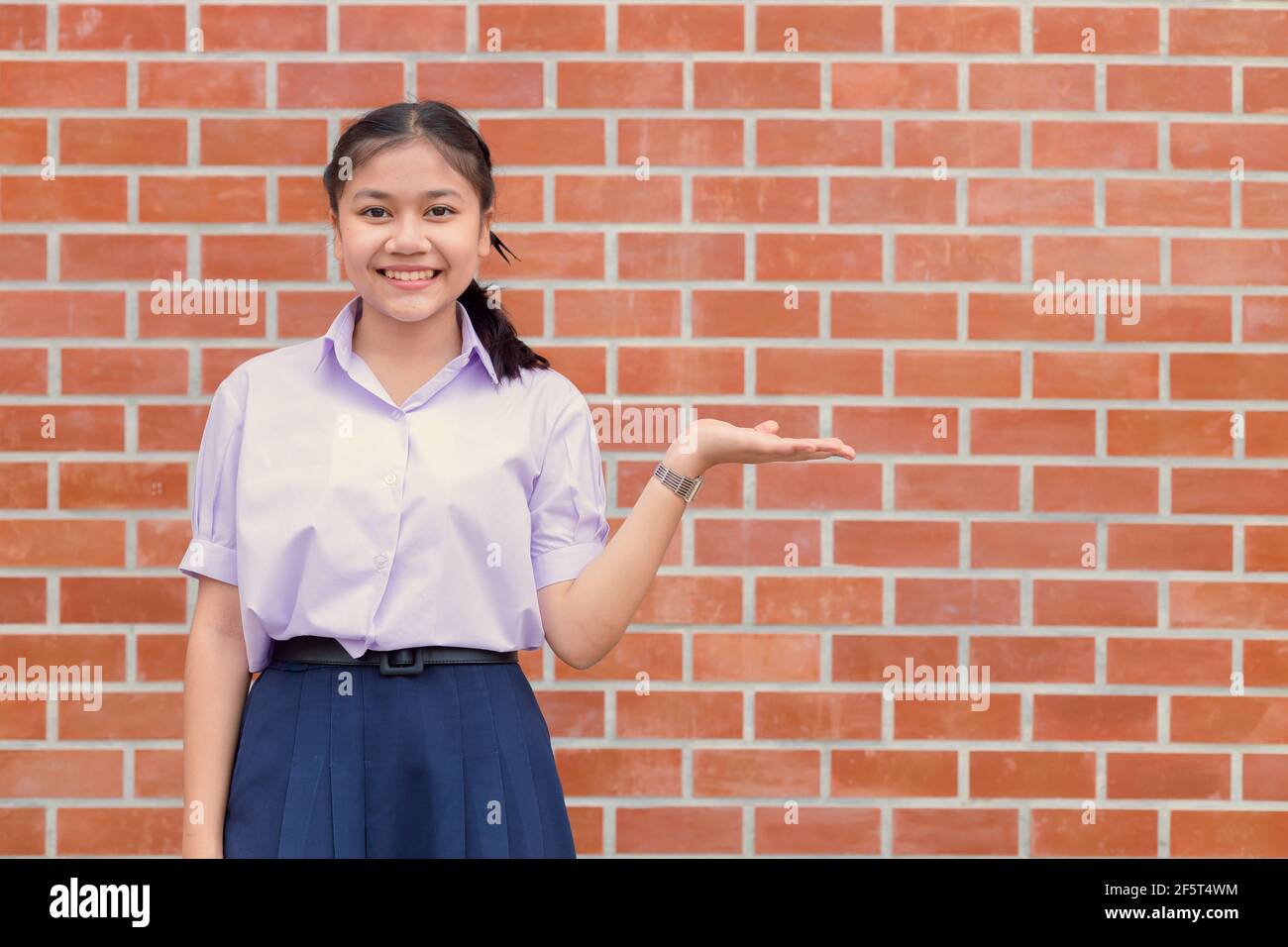 Asian ragazza teen studente uniforme sorriso felice con il presentante di mano che mostra spazio di copia della parete di esposizione. Foto Stock